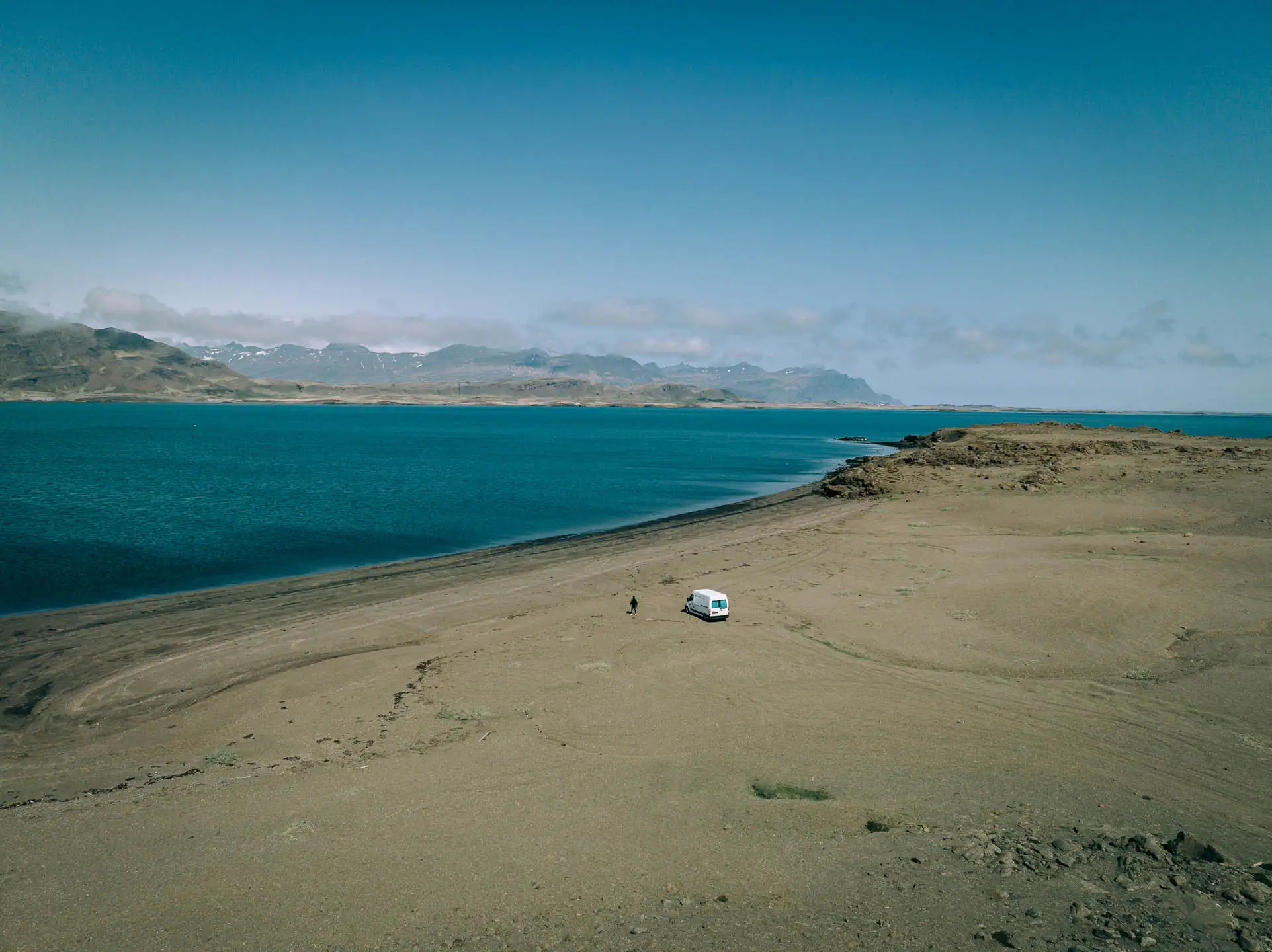 White Fiat Ducato campervan parked on sandy Iceland beach with turquoise ocean and snow-capped mountains in distance