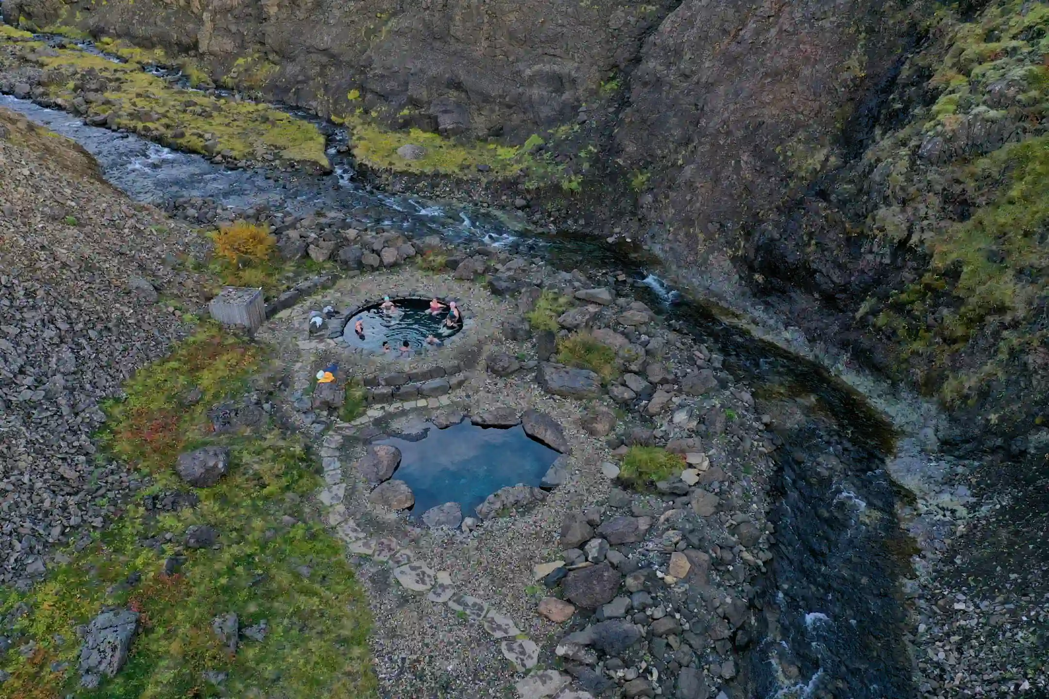 Aerial view of natural stone hot spring pools in Iceland beside a river in a rocky valley.