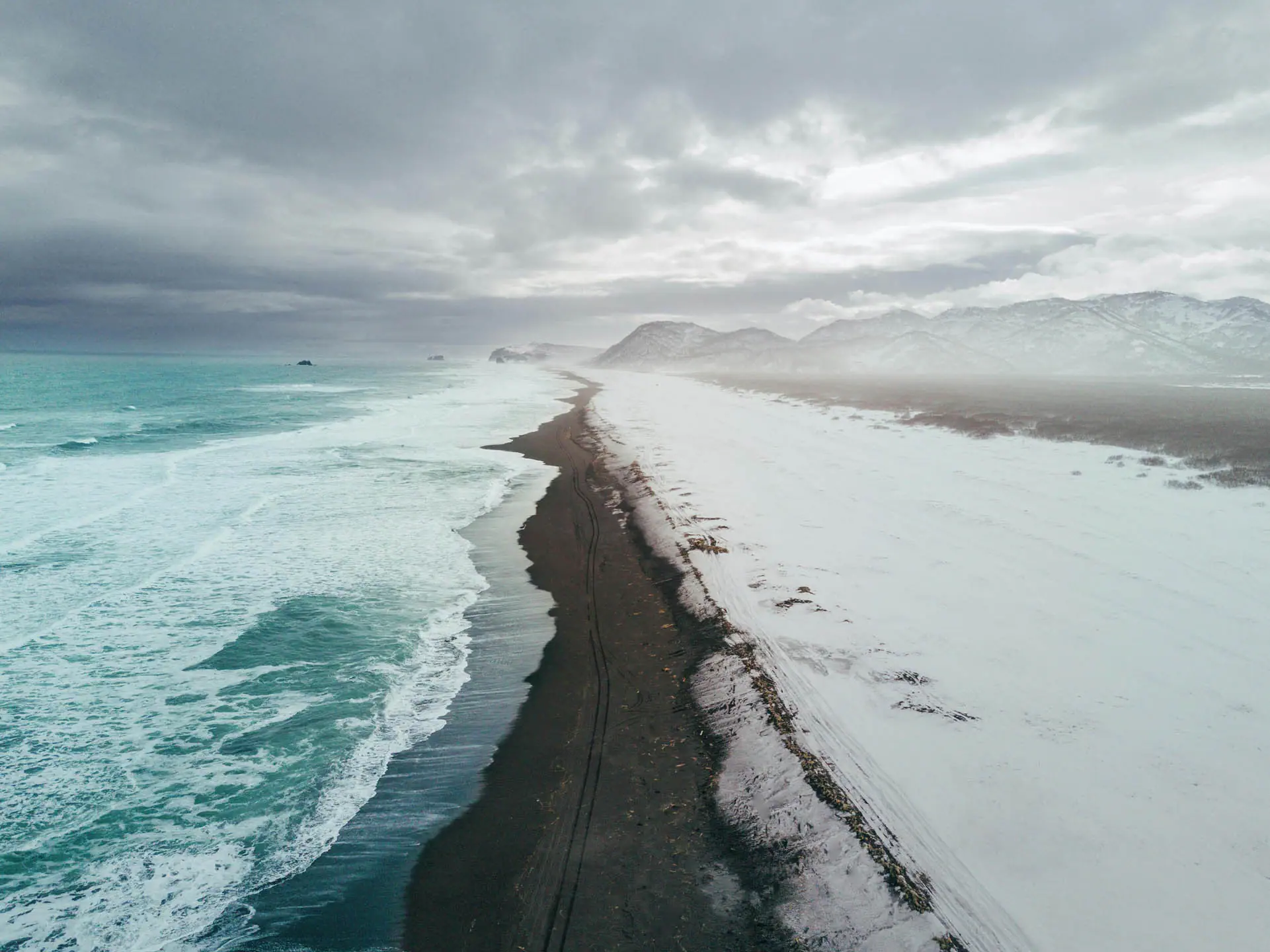 Driving a campervan along a snowy black sand beach in Iceland in winter