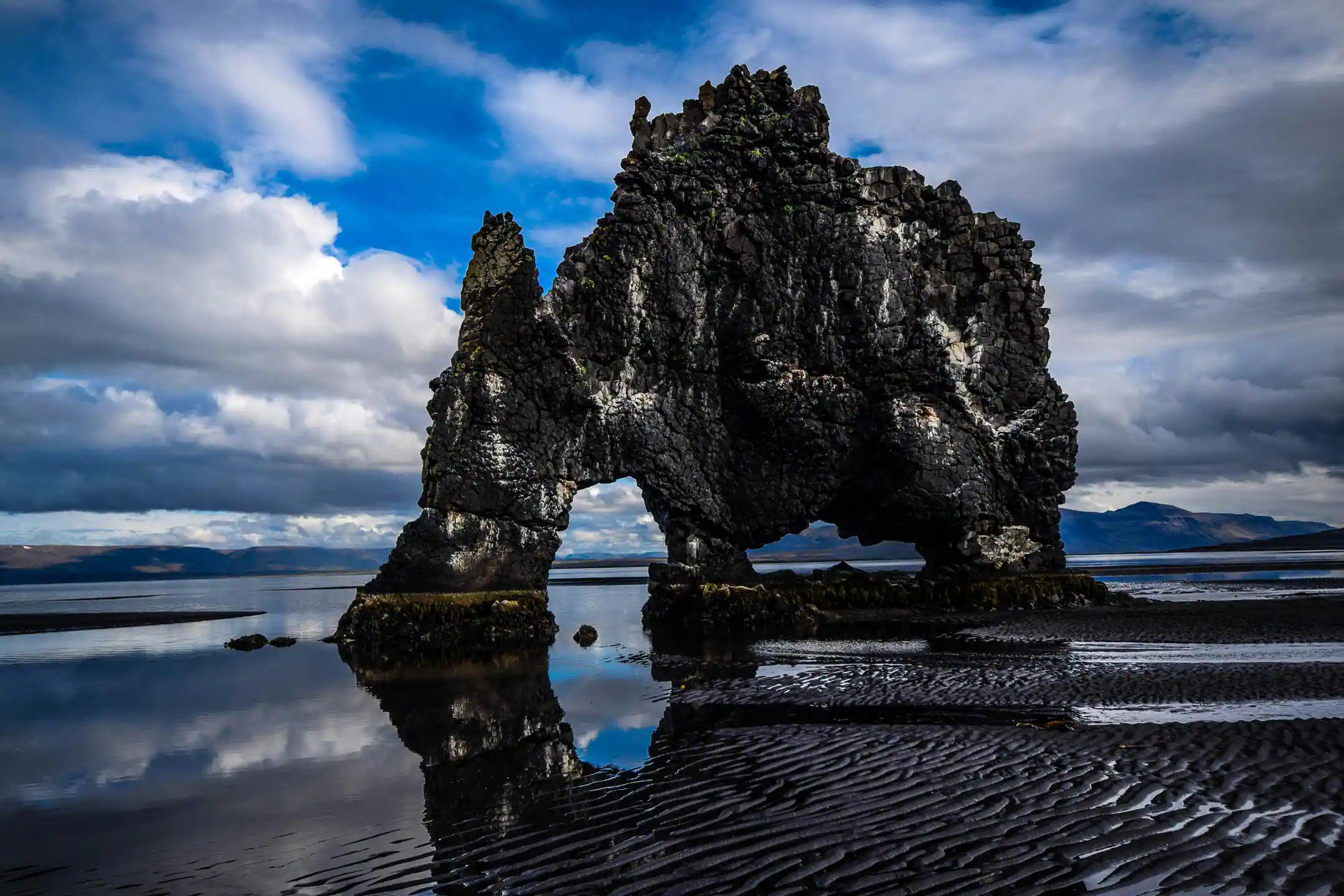 Hvítserkur basalt sea stack reflected in wet sand under dramatic clouds in northwestern Iceland, along a strong eclipse travel region.