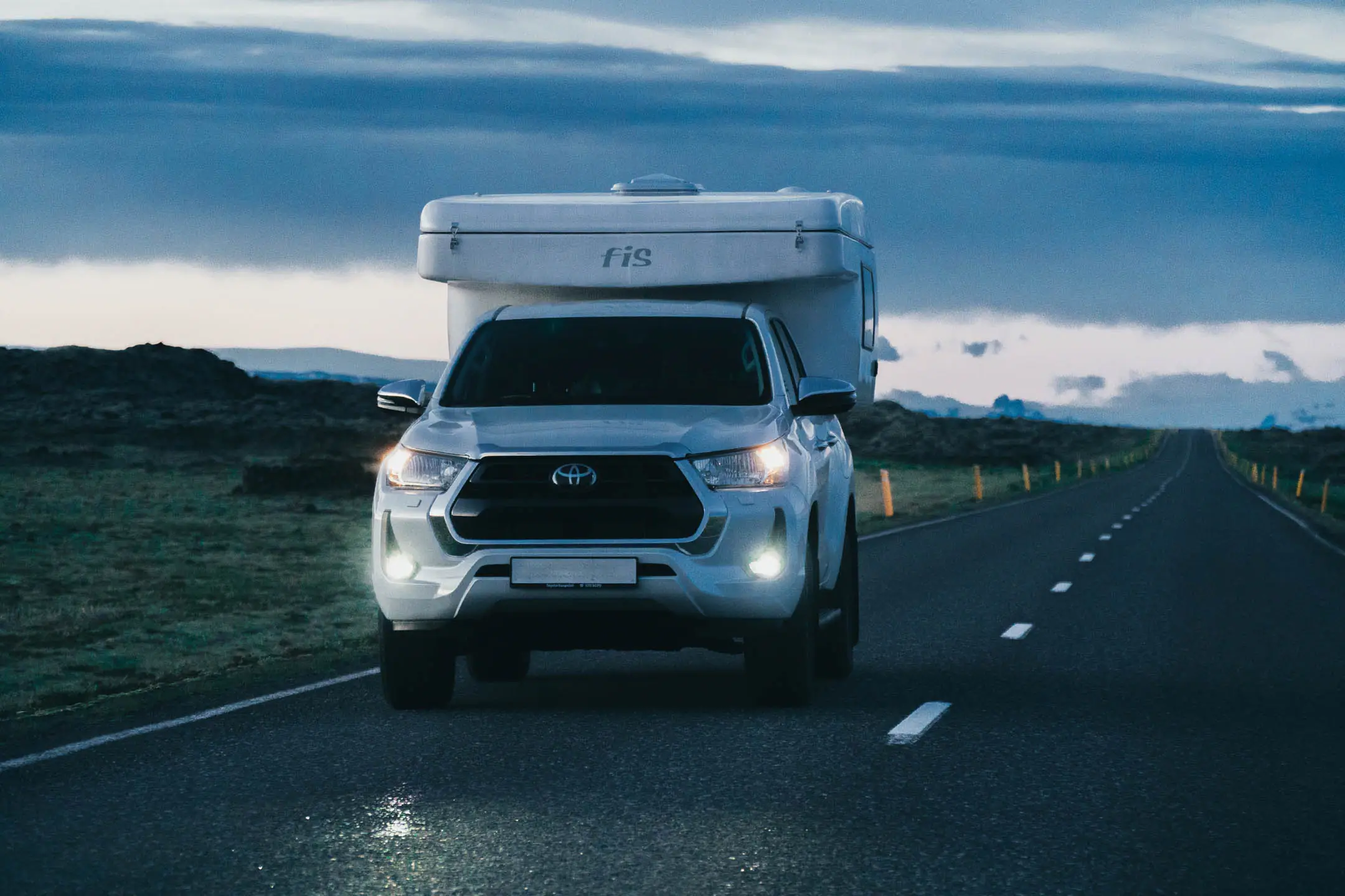oyota Hilux campervan driving along an empty Icelandic road at dusk, a classic scene on an Iceland campervan itinerary.