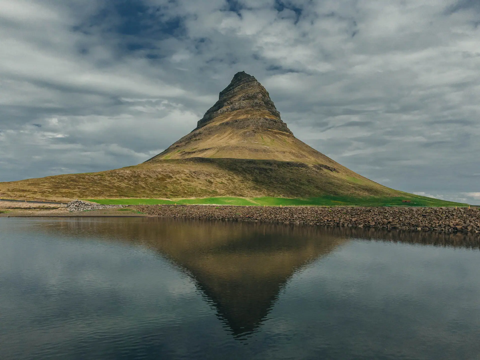 Kirkjufell mountain reflected in still water under a cloudy Icelandic sky, one of the most famous landmarks near the 2026 eclipse path.
