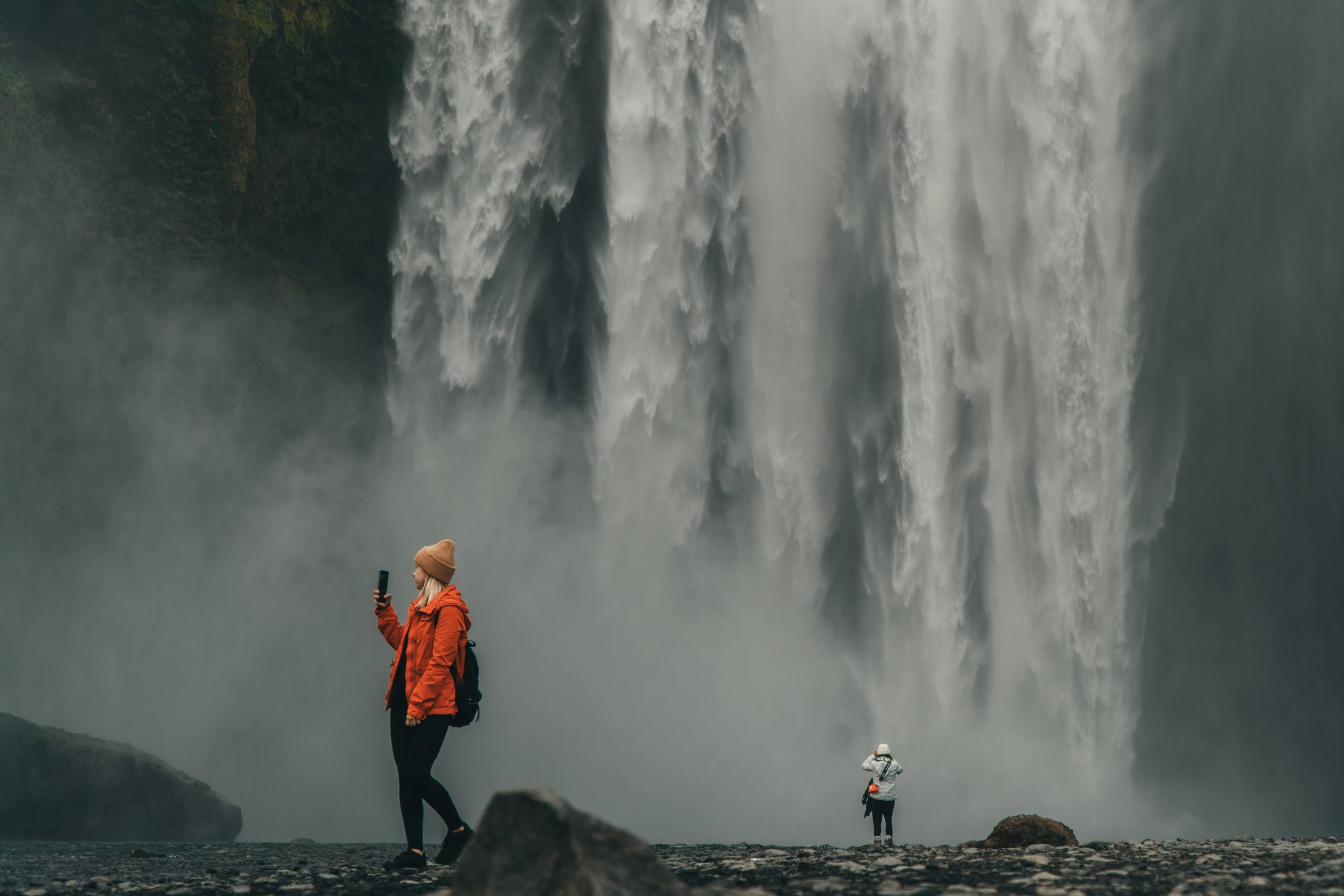 Tourist using a smartphone for internet and navigation near a large waterfall in Iceland, showing the importance of mobile data and connectivity while traveling.