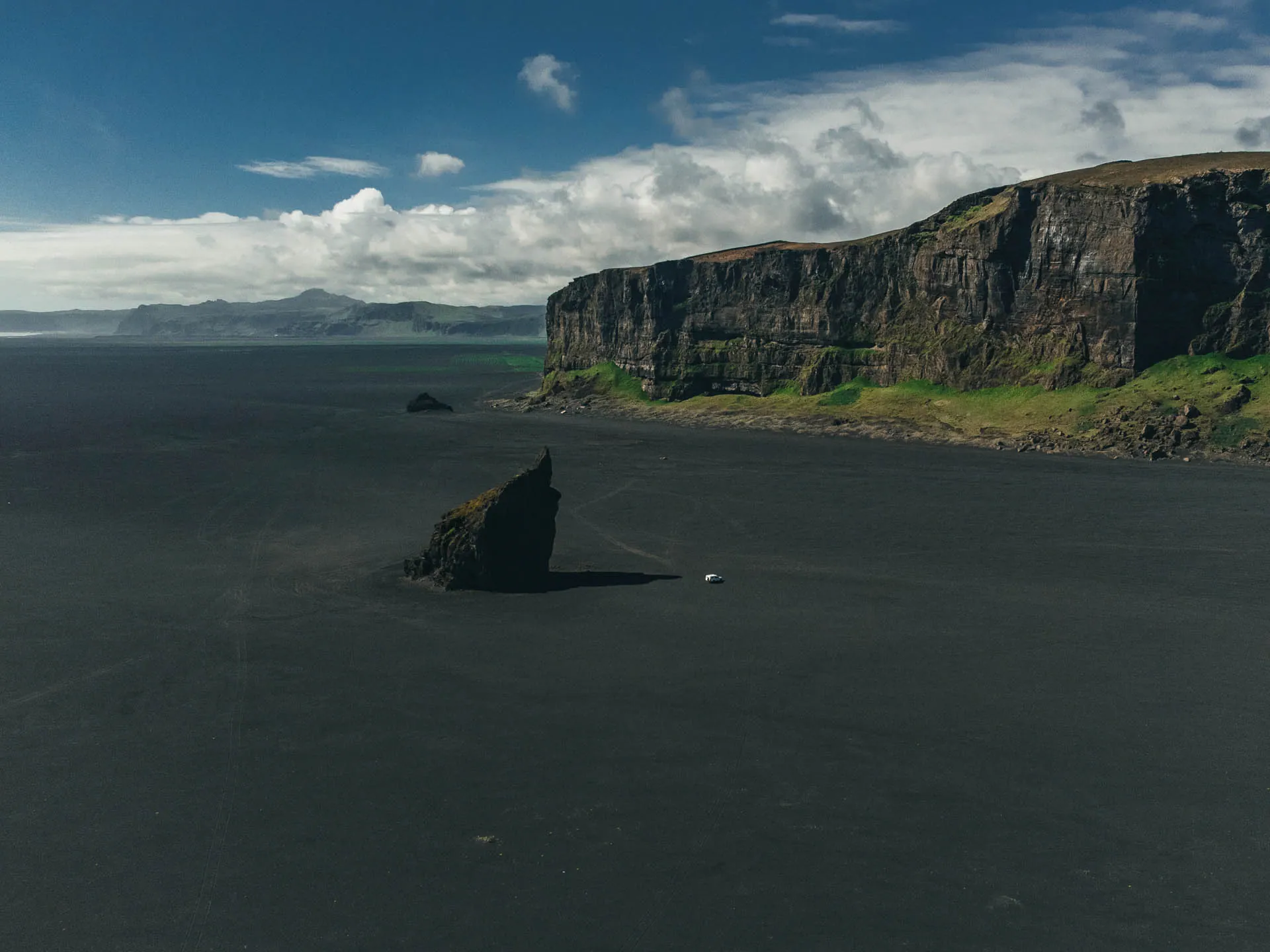 Campervan safety in Iceland shown on a black sand beach with steep cliffs and a vehicle driving in a remote coastal area