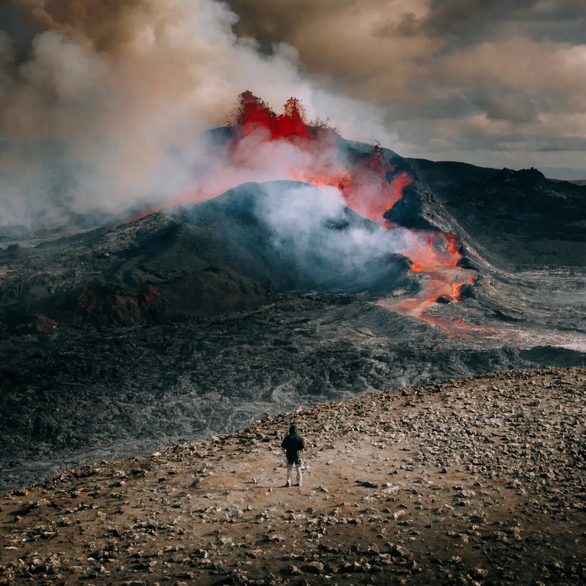 Person standing at a safe distance observing an active volcanic eruption in Iceland, with flowing lava, glowing magma, and thick volcanic smoke rising from the crater near Grindavík